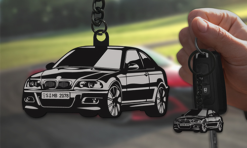 Car keychain shaped like black BMW E46 held in hand, racetrack with red-white car in background