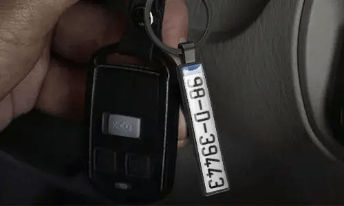 Zilveren nummerplaat sleutelhanger hangt aan autosleutels in het voertuig