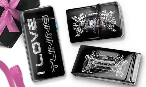 Drei glänzende Auto-Accessoires sind auf weißem Hintergrund zu sehen. Eines trägt die Aufschrift „I Love Tuning“, ein anderes zeigt Vintage-Rennmotive und das letzte ein blaues Sportauto mit Motor-Motiven. Eine rosa Schleife ist teilweise sichtbar.