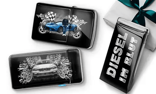 Two sleek black lighters featuring car themes, one with a blue car and checkered flags, another with a red car and gears. A third lighter reads 'DIESEL IM BLUT'. Gift-wrapped in the background.